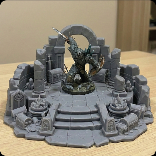 A tabletop miniature display featuring a fantasy creature figurine posed in a ruined stone arena with stairs, arches, crates, and debris, photographed on a light wood surface against a beige indoor background.