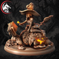 A fantasy tabletop miniature sculpture of a witch riding a pumpkin-skull creature on a round base, shown against a dark spooky tree background. A red and black dragon-head logo appears in the top-left corner.