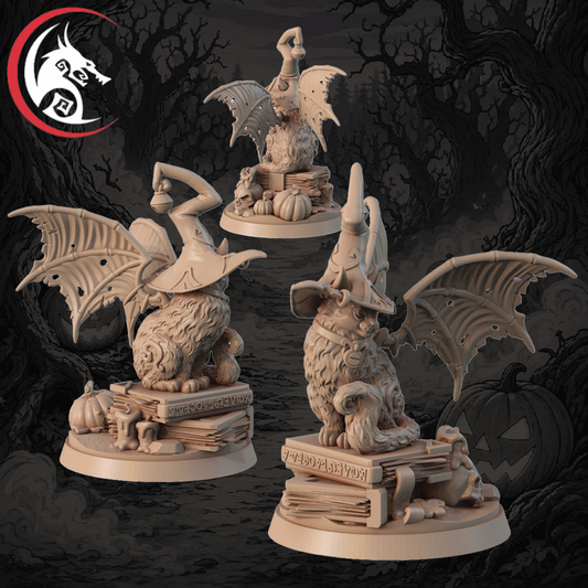 Three unpainted fantasy tabletop miniatures displayed against a dark illustrated background. The figures are light beige resin or plastic models featuring a goblin-like creature with large bat wings, sitting on stacks of books with pumpkins and a small skull.