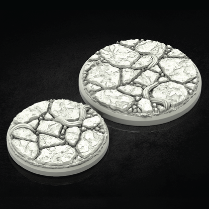 Two round 3D-printed terrain bases with a cracked stone texture and a winding river detail, shown on a dark reflective background.