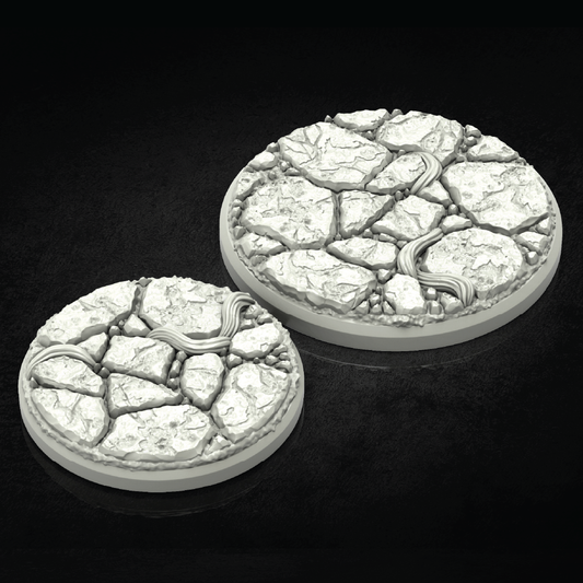 Two round 3D-printed terrain bases with a cracked stone texture and a winding river detail, shown on a dark reflective background.