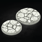 Two round 3D-printed terrain bases with a cracked stone texture and a winding river detail, shown on a dark reflective background.