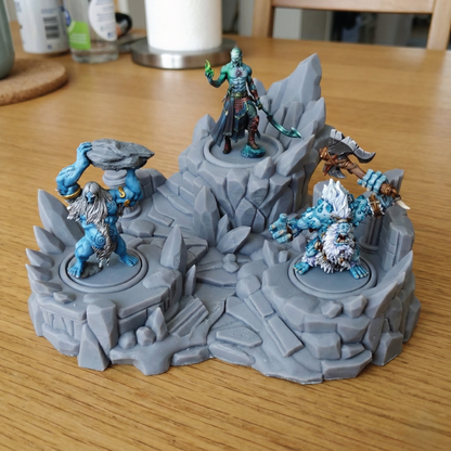 A gray fantasy tabletop terrain piece with four painted miniature figures on circular bases, photographed on a wooden table in a home setting.