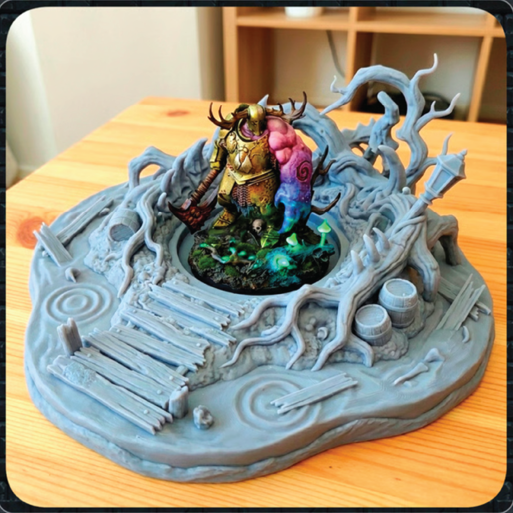 A 3D-printed tabletop miniature display base featuring a fantasy warrior figurine with a colorful pink and blue creature, set on a gray tree-root themed base on a wooden table.