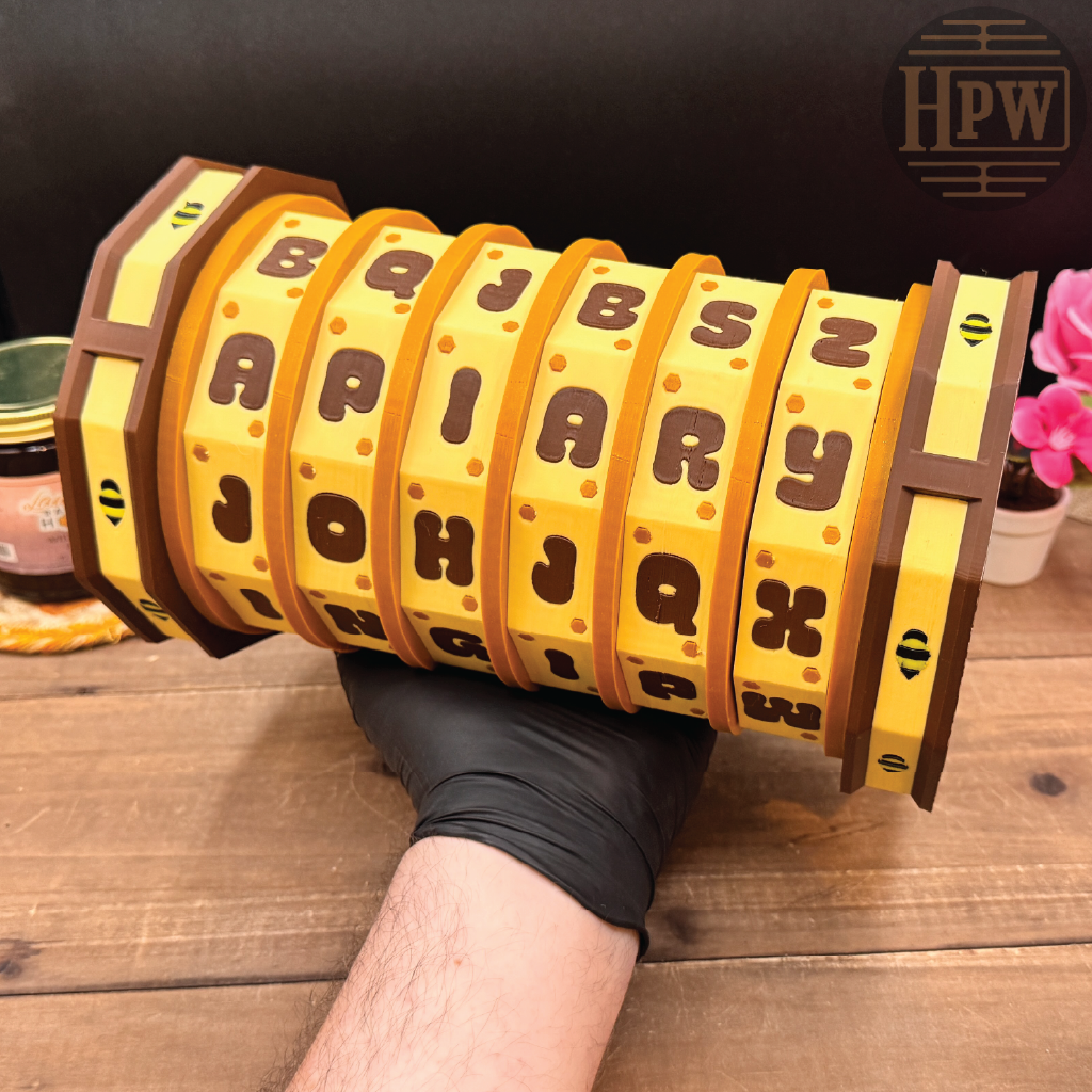 Yellow cylindrical object with letter labels held by a gloved hand on a wooden surface, with 'HPW' branding.