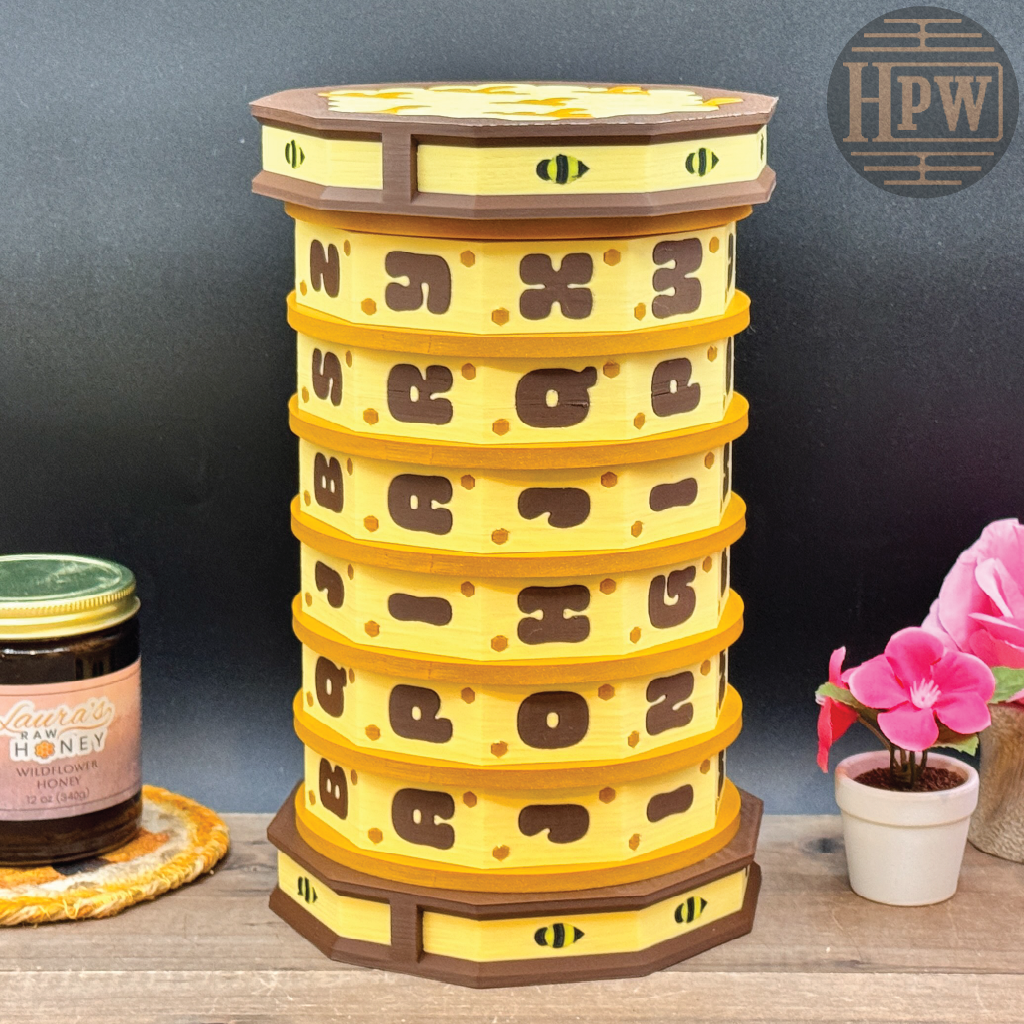 Yellow honeycomb-shaped container with brown accents on a wooden surface, next to a jar of honey and a plant.