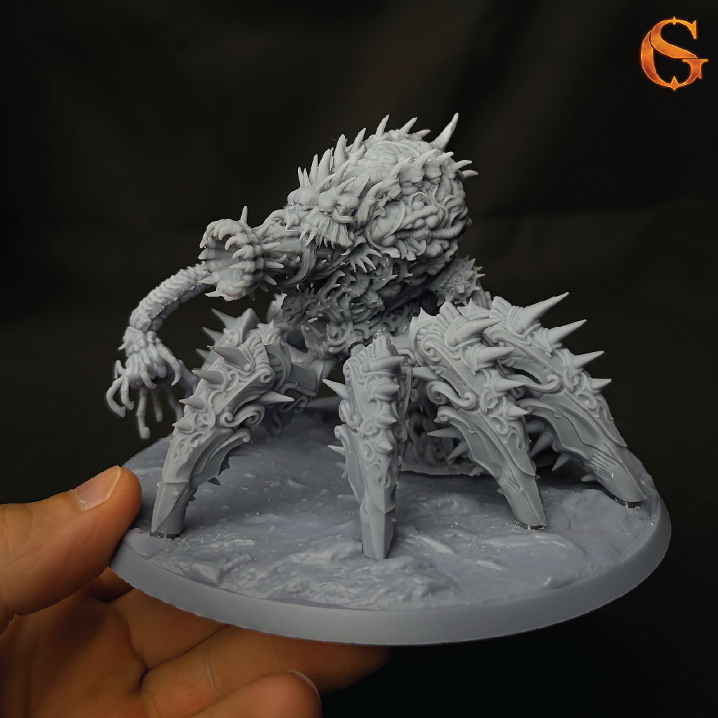 A gray unpainted fantasy monster miniature on a round base, held in a person's hand against a dark background. The creature has multiple spiky legs and a detailed textured body.