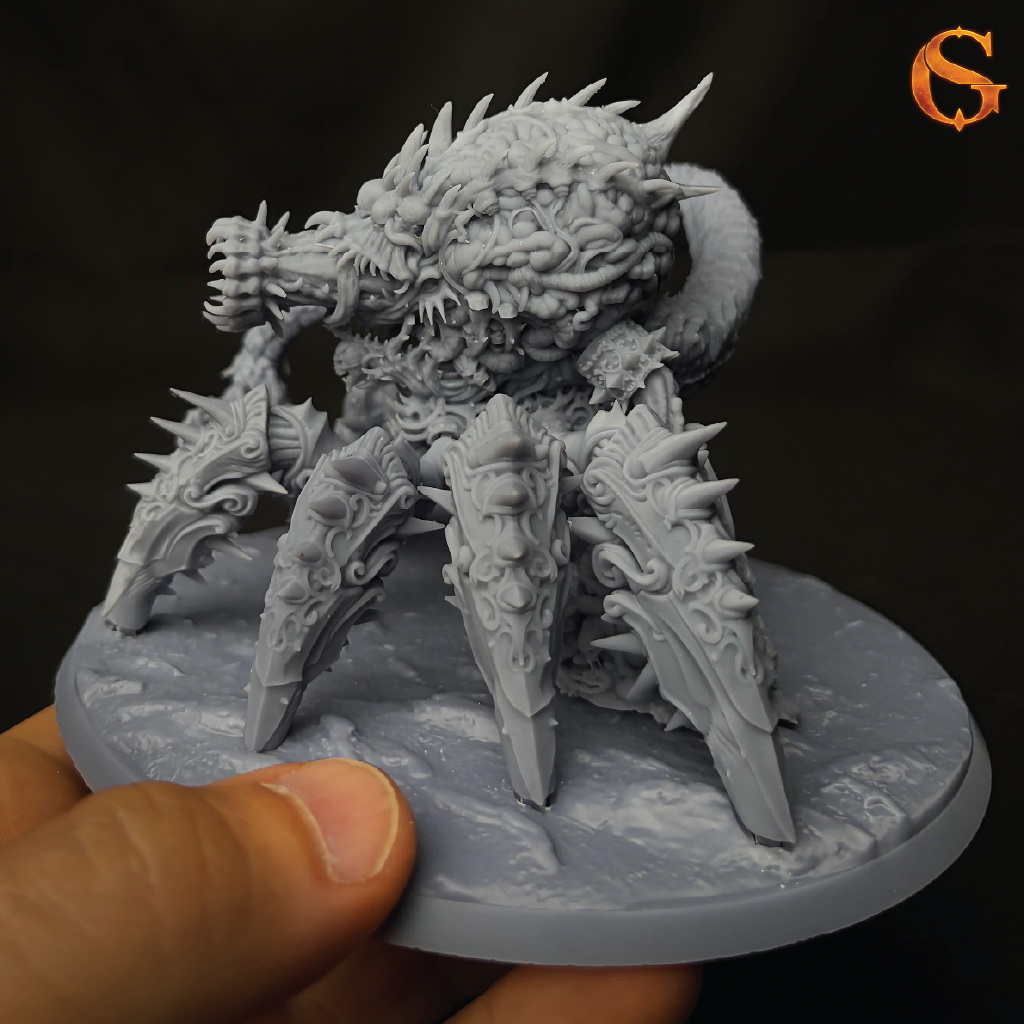 A hand holding an unpainted gray fantasy monster miniature on a round base against a dark background, with an orange stylized 'S' logo in the top right corner.