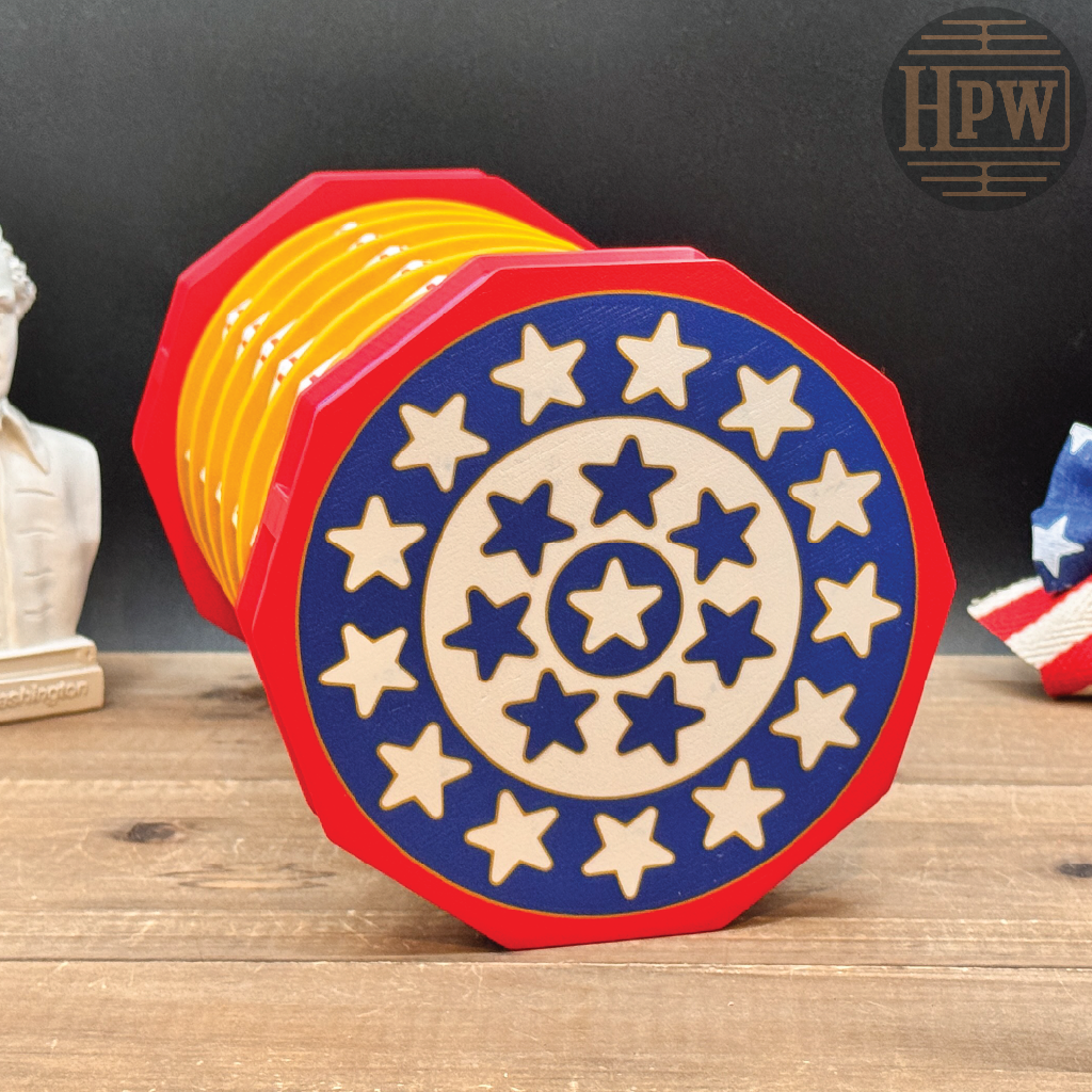 A red, white, and blue octagonal wooden coaster or decorative block with a circular star pattern, shown standing on a wooden surface against a dark background. A small HPW logo appears in the top right corner.