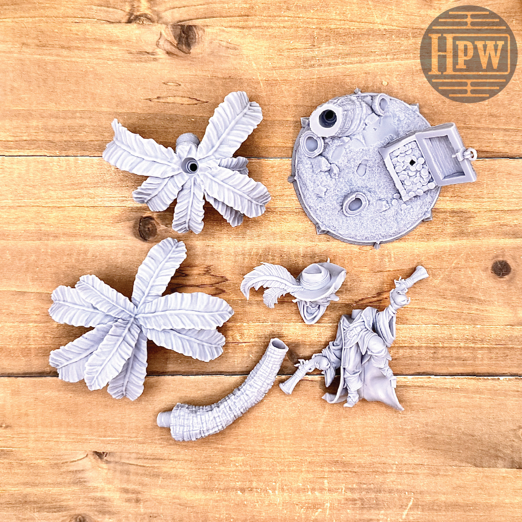 The parts for a goblin pirate wielding miniature blunderbusses standing under a palm tree and on top of an open treasure chest full of coins. This is a model 3D printed in gray UV resin.