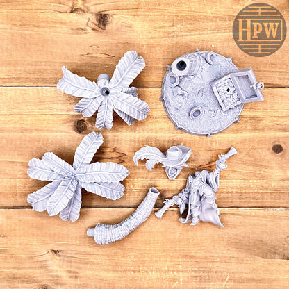 The parts for a goblin pirate wielding miniature blunderbusses standing under a palm tree and on top of an open treasure chest full of coins. This is a model 3D printed in gray UV resin.
