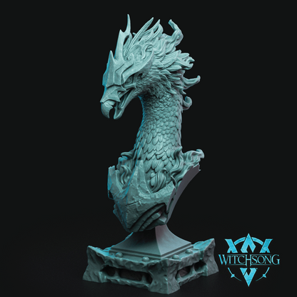 A detailed fantasy bust sculpture of a dragon head on a pedestal base, shown in a light teal-blue color against a solid black background. A 'WITCHSONG' brand logo is visible in the bottom right corner.