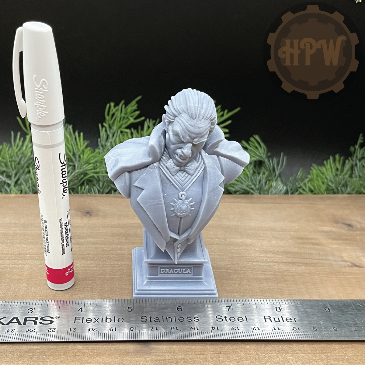 A light gray 3D-printed bust of Dracula on a display stand, shown next to a white Sharpie marker and a metal ruler for scale on a wooden surface.