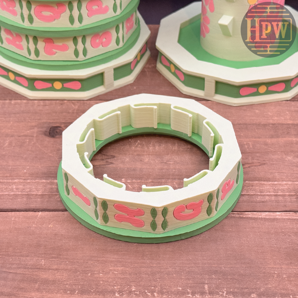 Decorative paper cake stand with pink and green design on a wooden surface, featuring the brand 'HPW'.
