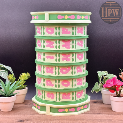 Decorative tower with pink and green design on a wooden surface with plants.