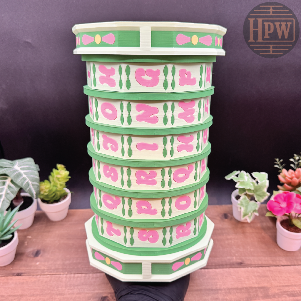 Stack of decorative planters with pink and green design on a wooden surface.