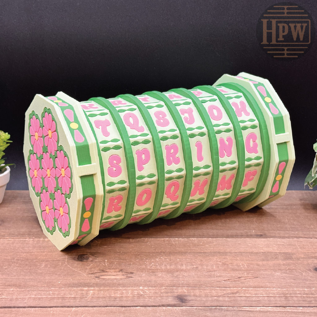 Decorative wooden box with floral and letter designs on a wooden surface, branded 'HPW'.