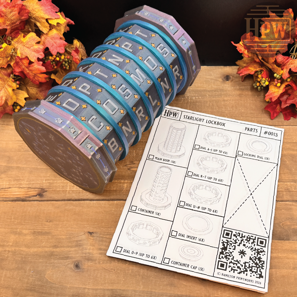 A cylindrical starlight lockbox with rotating letter bands in a galaxy pattern, displayed next to its parts instruction sheet on a wooden tabletop with autumn leaves.