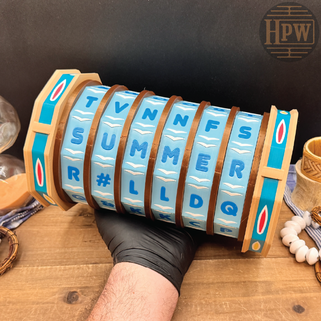 A hand wearing a black glove holds a cylindrical wooden letter wheel puzzle with turquoise blue letter tiles spelling out summer months, set on a rustic wooden table with a dark background.