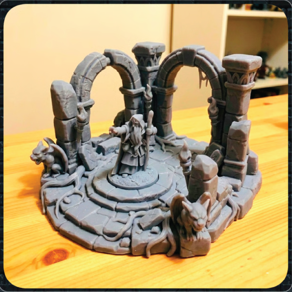 A gray unpainted 3D-printed tabletop miniature terrain piece depicting a fantasy stone arena with arches, a central platform, and small creature figures, displayed on a wooden tabletop.