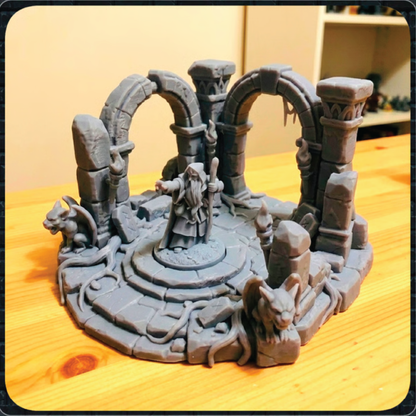 A gray unpainted 3D-printed tabletop miniature terrain piece depicting a fantasy stone arena with arches, a central platform, and small creature figures, displayed on a wooden tabletop.